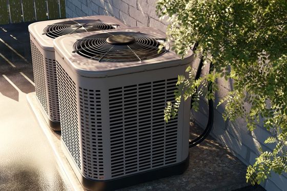 Outdoor air conditioning units beside a house wall, with sunlight and tree shadows nearby