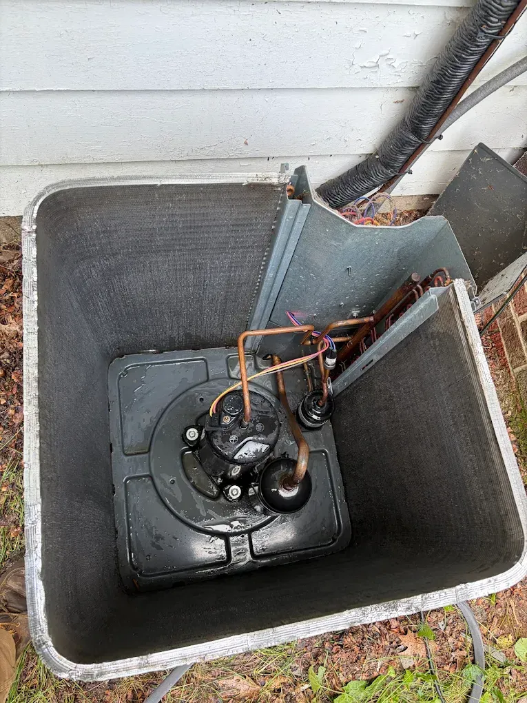 Open sump pit with pump and copper pipes beside a house wall
