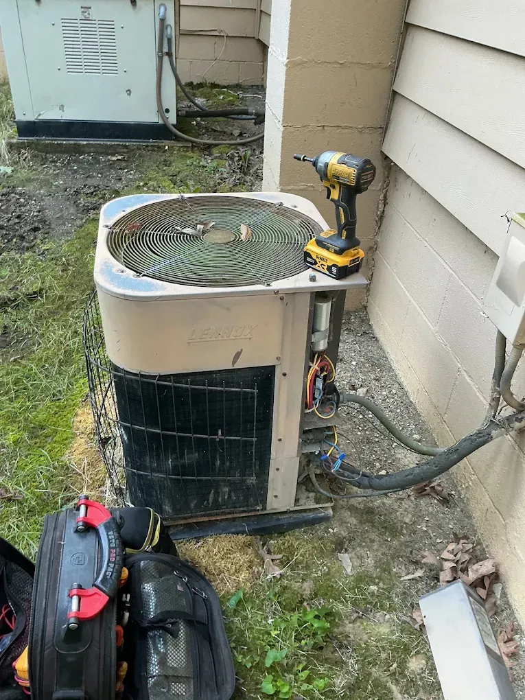 Outdoor air conditioner unit with tools attached beside a house wall.