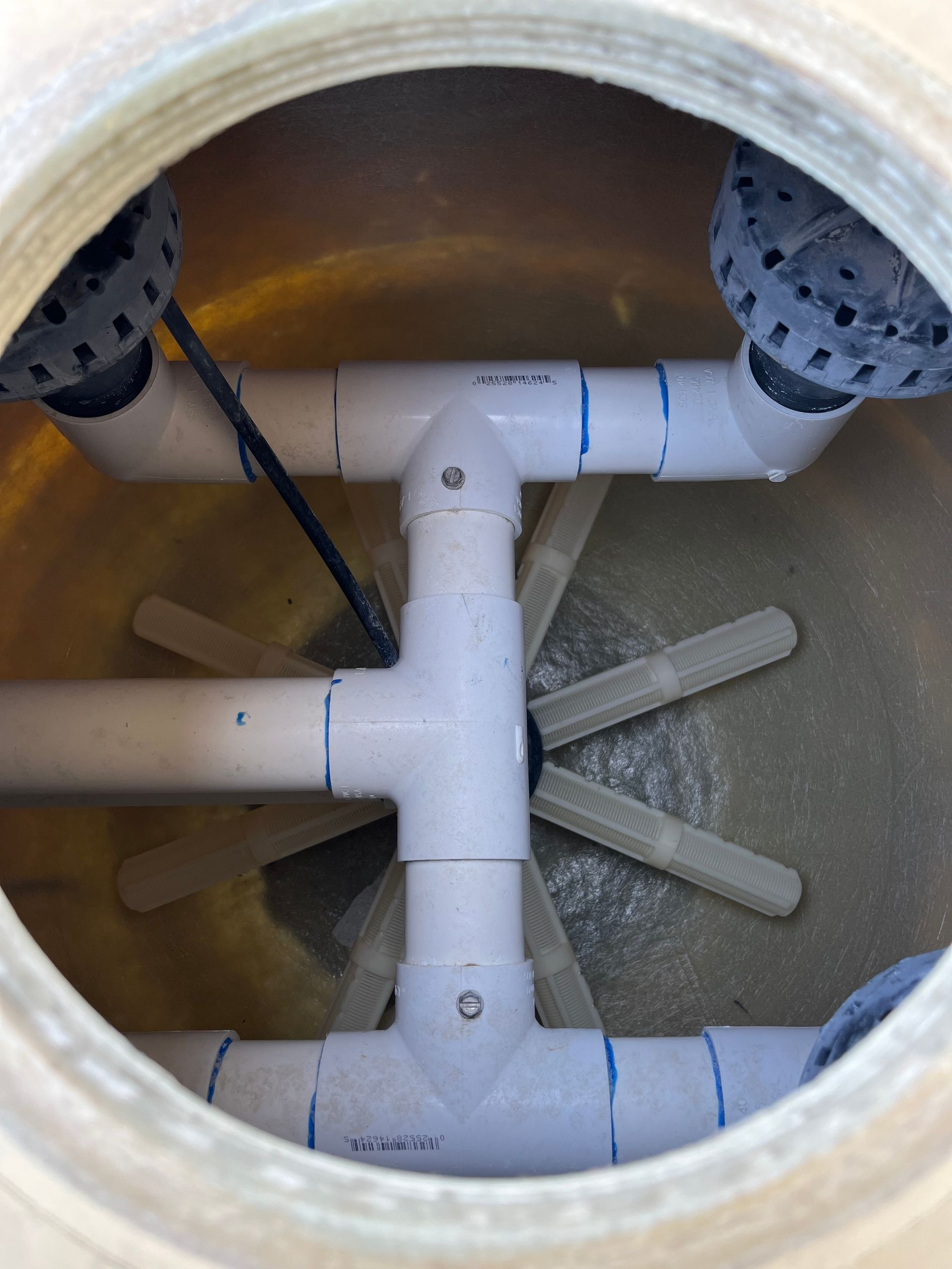 Inside view of a white PVC pipe structure with plastic diffusers inside a round, beige sand filter tank.