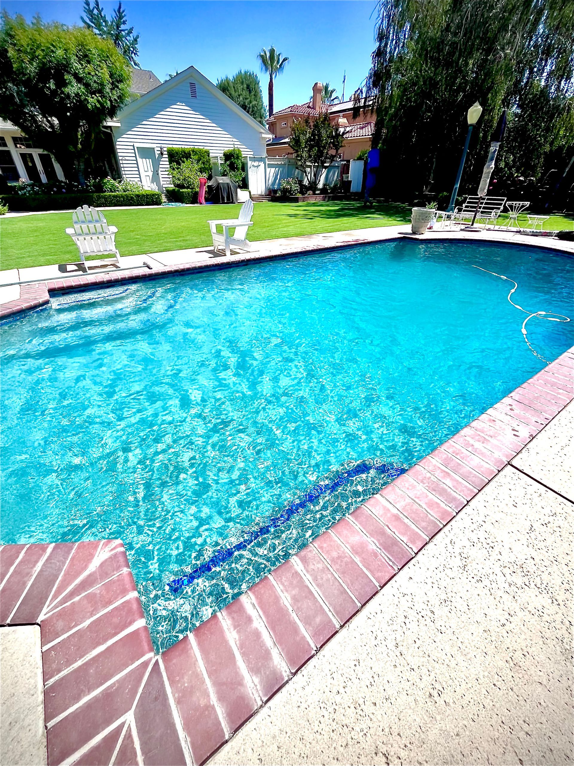 Blue swimming pool surrounded by brick and concrete, with a white gazebo and lawn in the background.