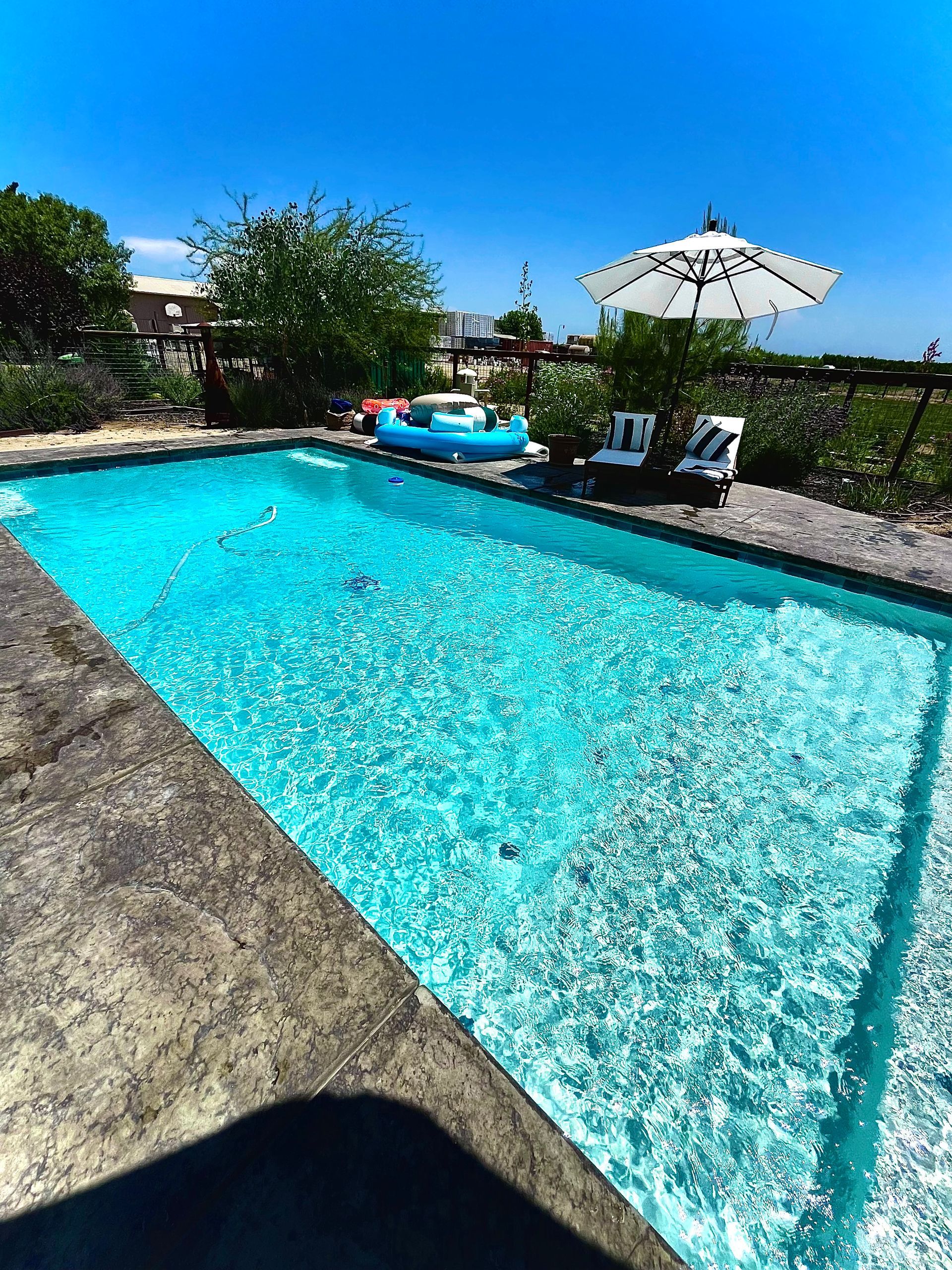 Pool with blue water, patio furniture, umbrella, and a blue inflatable boat. Sunny day.