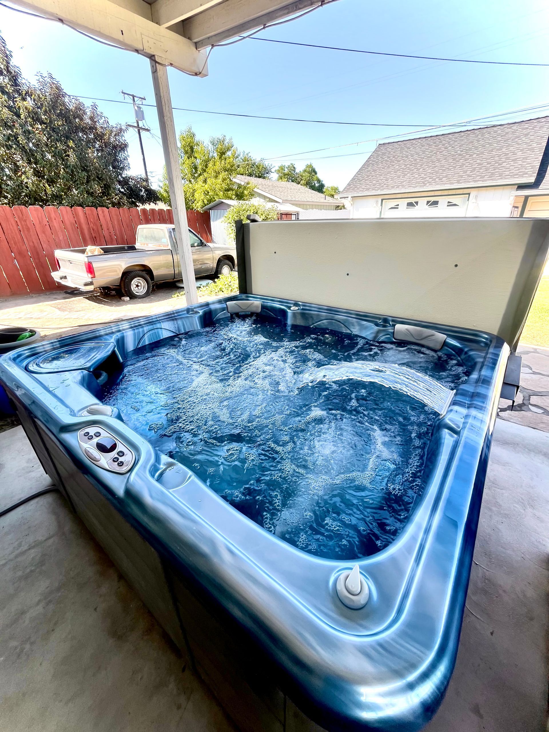 Hot tub filled with bubbly water, under a porch, truck in the background.