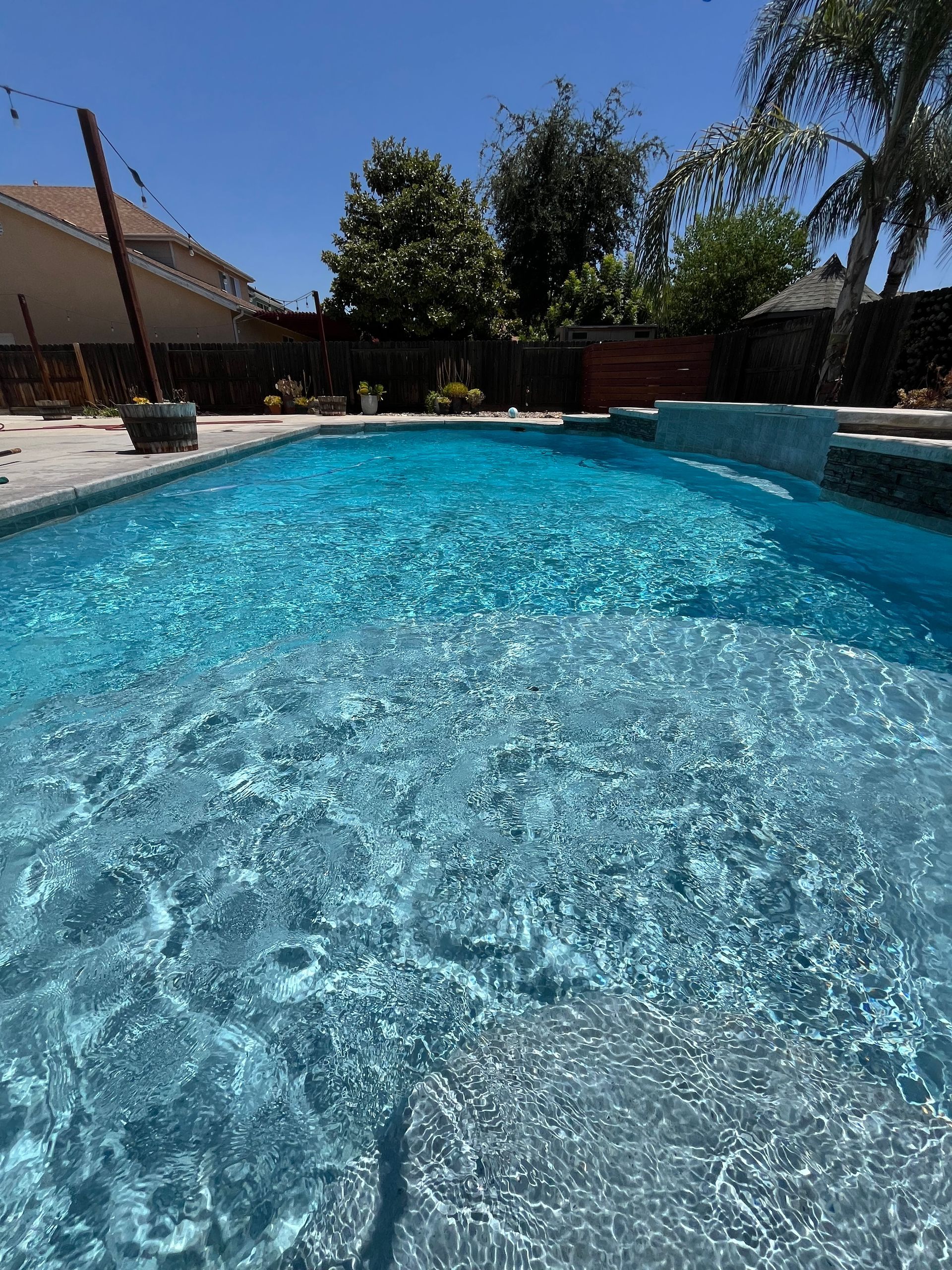 Blue, sunlit swimming pool with water rippling, backyard setting.