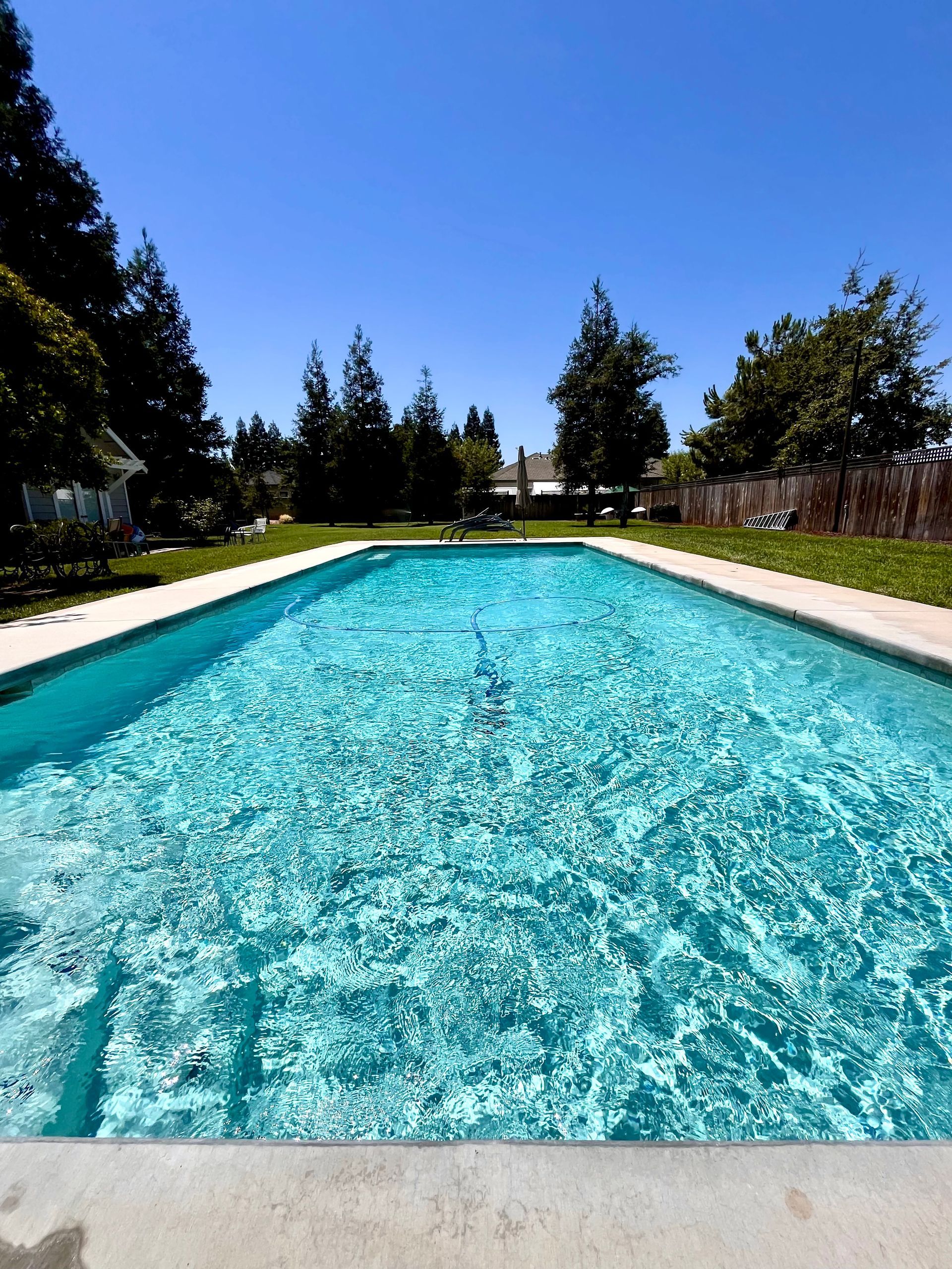 Rectangular pool with clear turquoise water, surrounded by concrete. Trees and blue sky in the background.