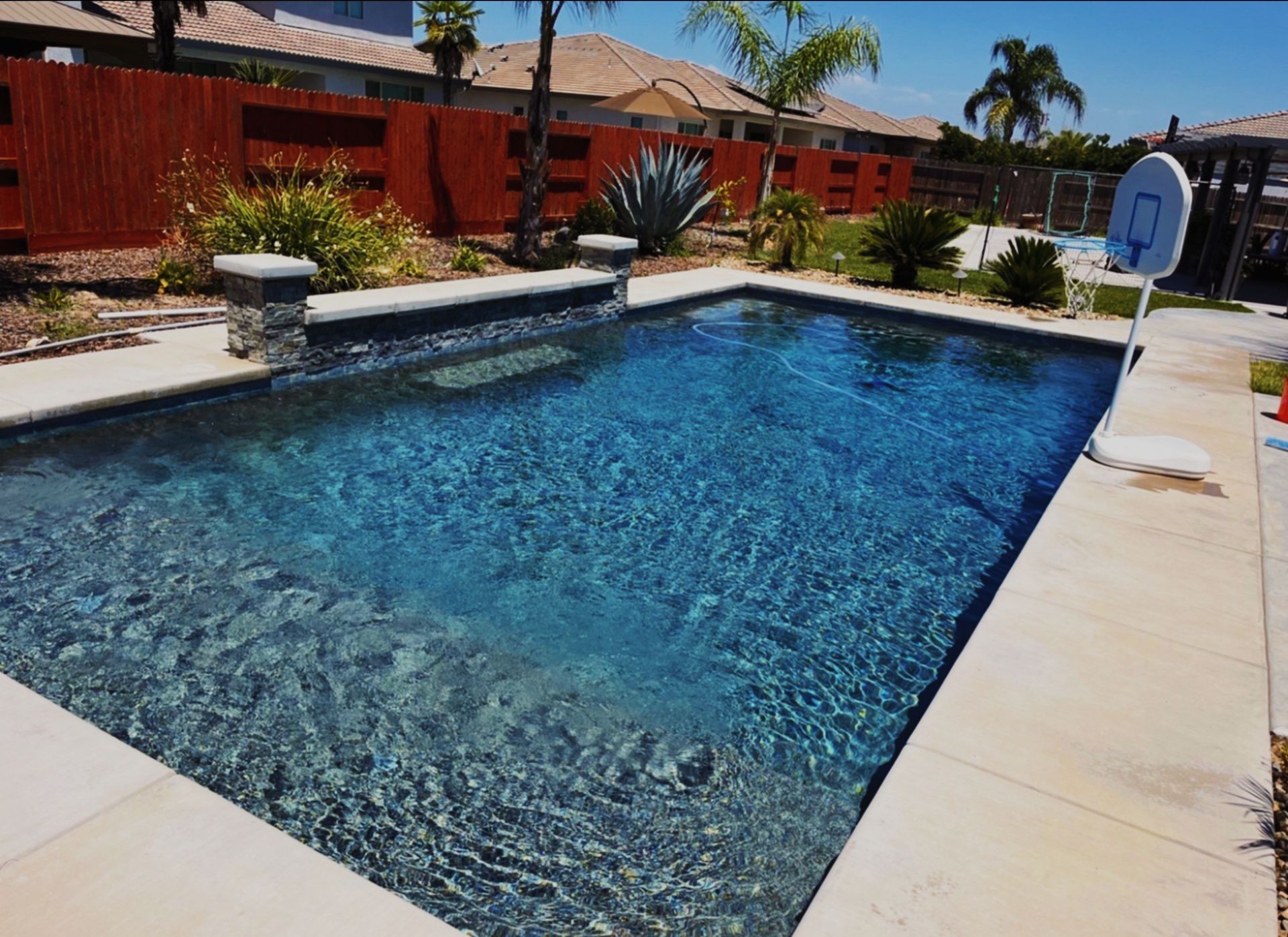 Rectangular pool with dark blue water, surrounded by light concrete. Bamboo fence in background.