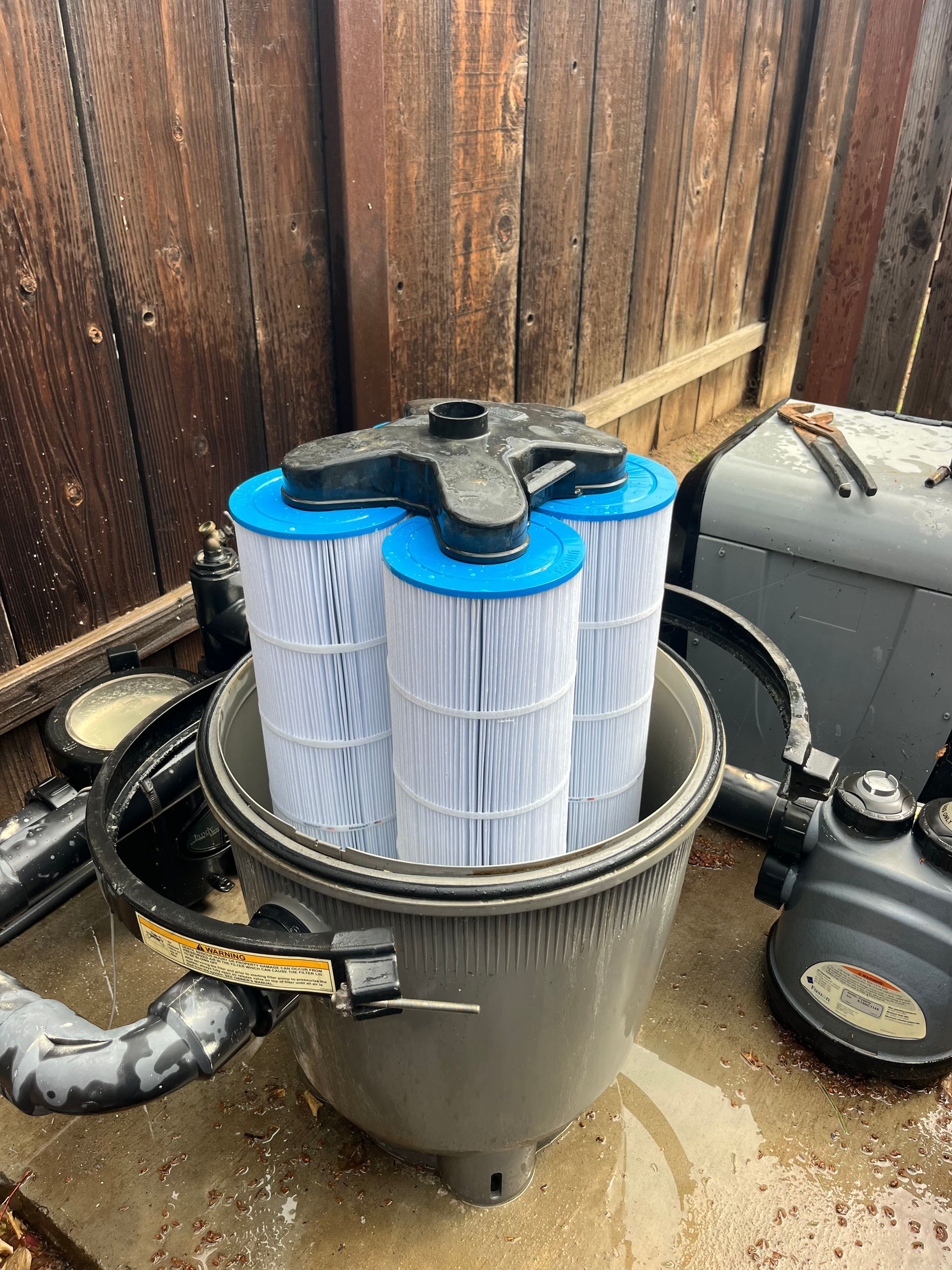 Pool filter with four cartridge filters inside a gray tank. Blue and white filter elements.