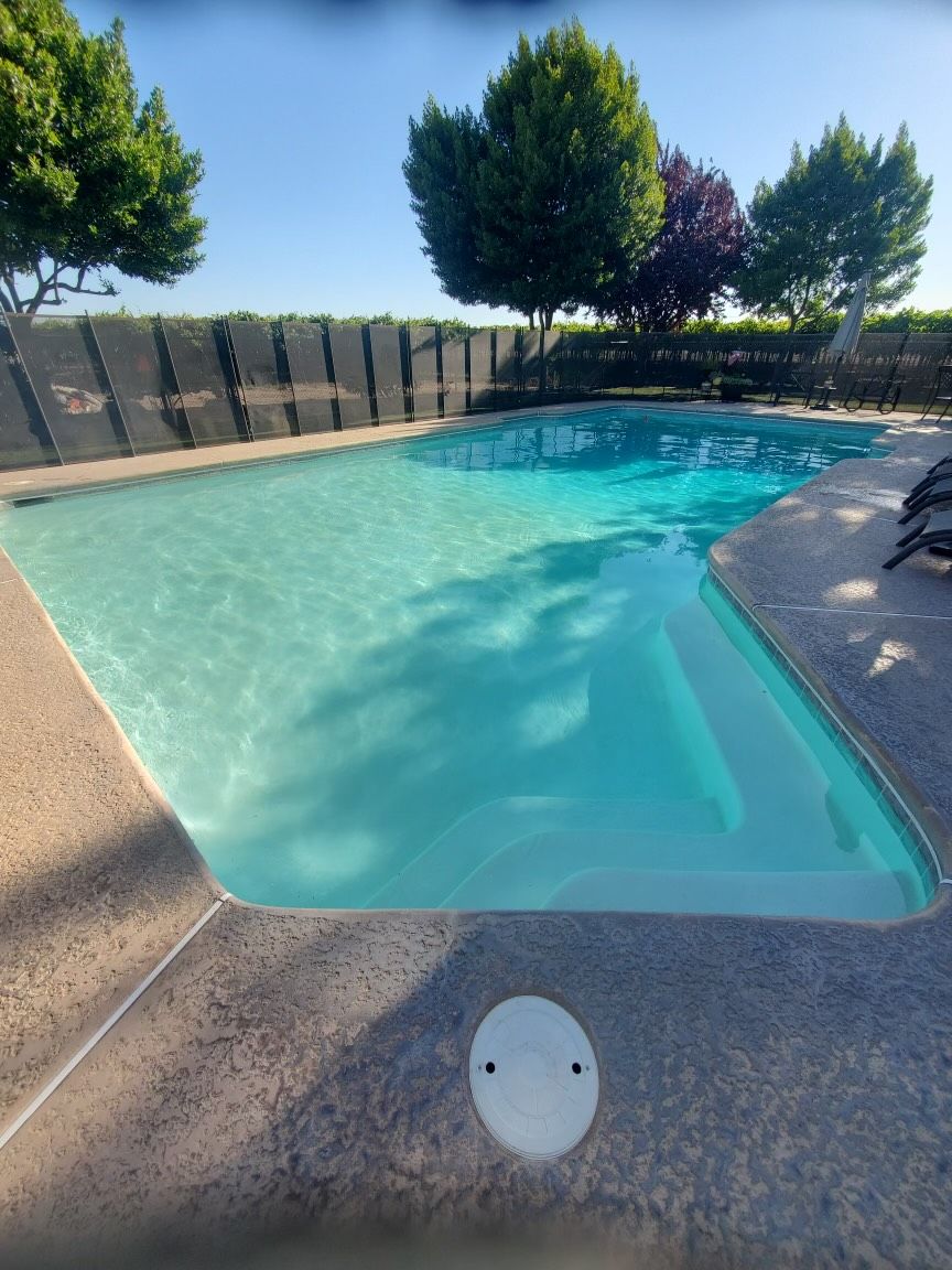 A clear swimming pool with concrete edges, trees in the background, blue water.
