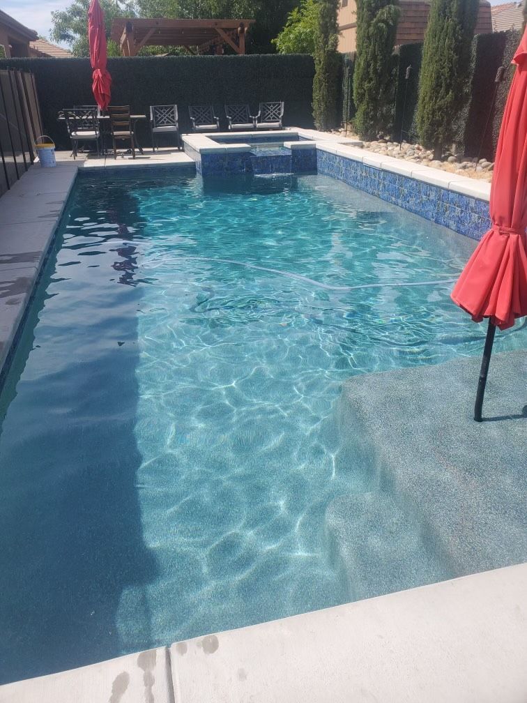 Rectangular swimming pool with blue tiles, steps, and a hot tub. Red umbrella visible.
