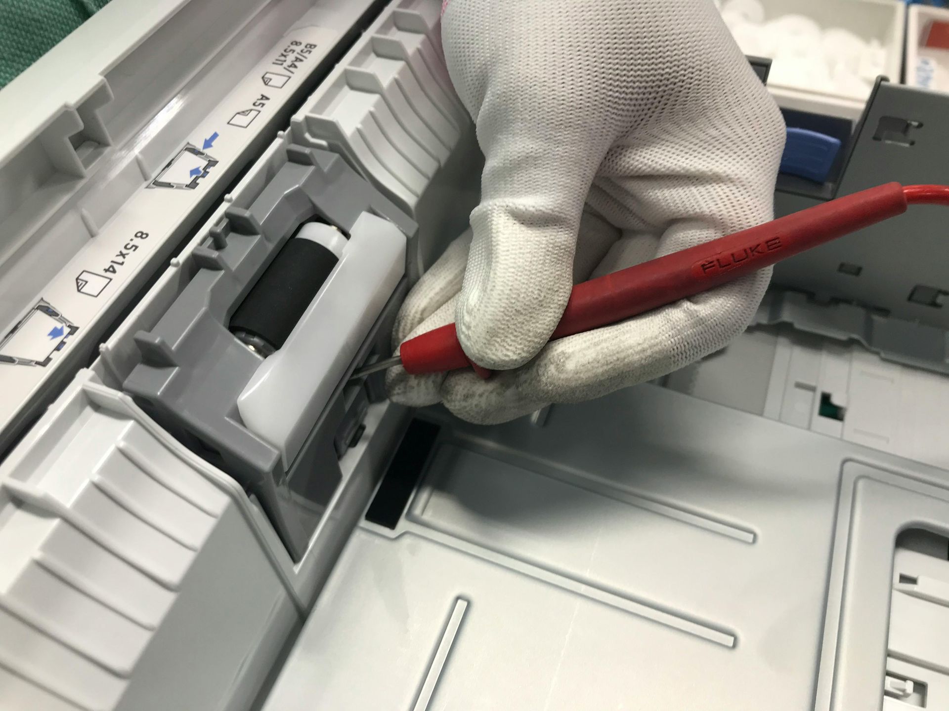 Gloved hand using a red tool to adjust a gray office device tray