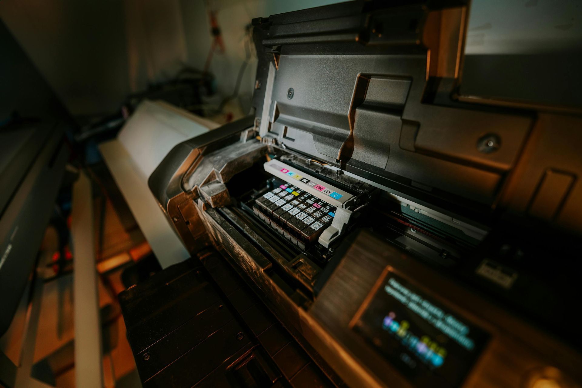 Wide-format printer with paper roll and colorful print head, in a dim workshop