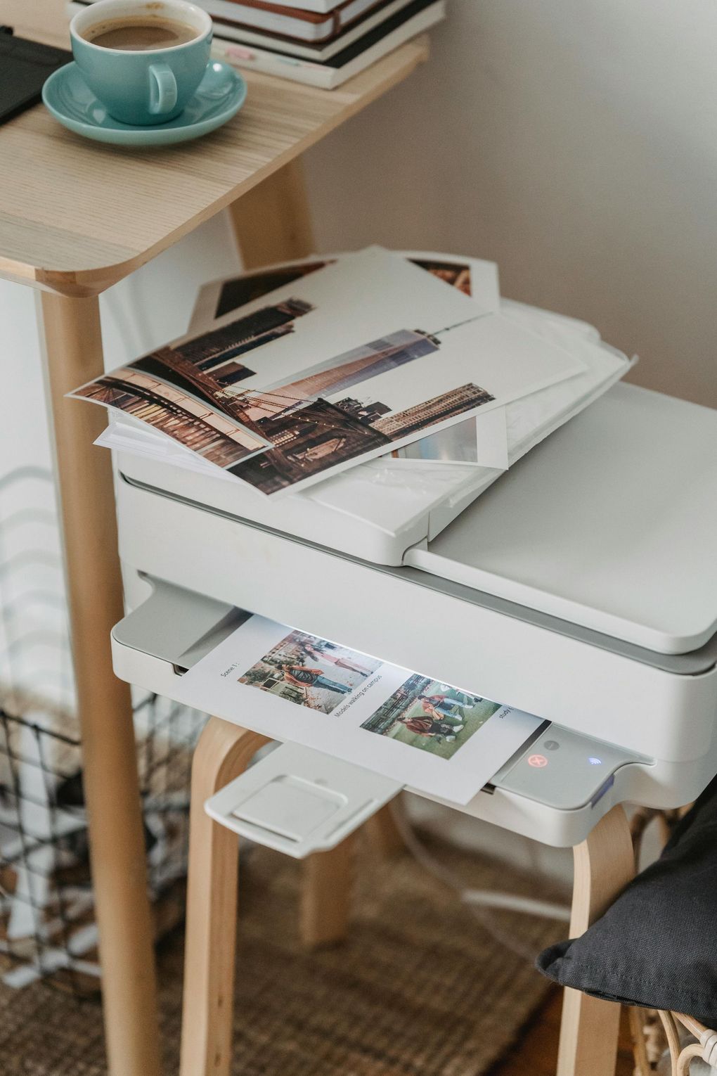 Printer with photo prints and a turquoise cup on a small table in a home office corner