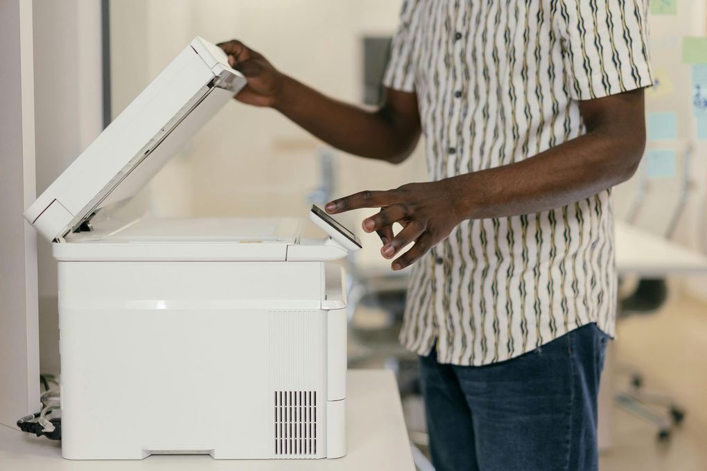 Person opening a white printer lid and removing paper in an office setting
