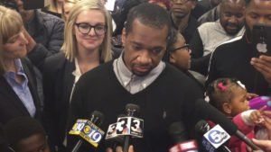 man is interviewed by crowd of reporters