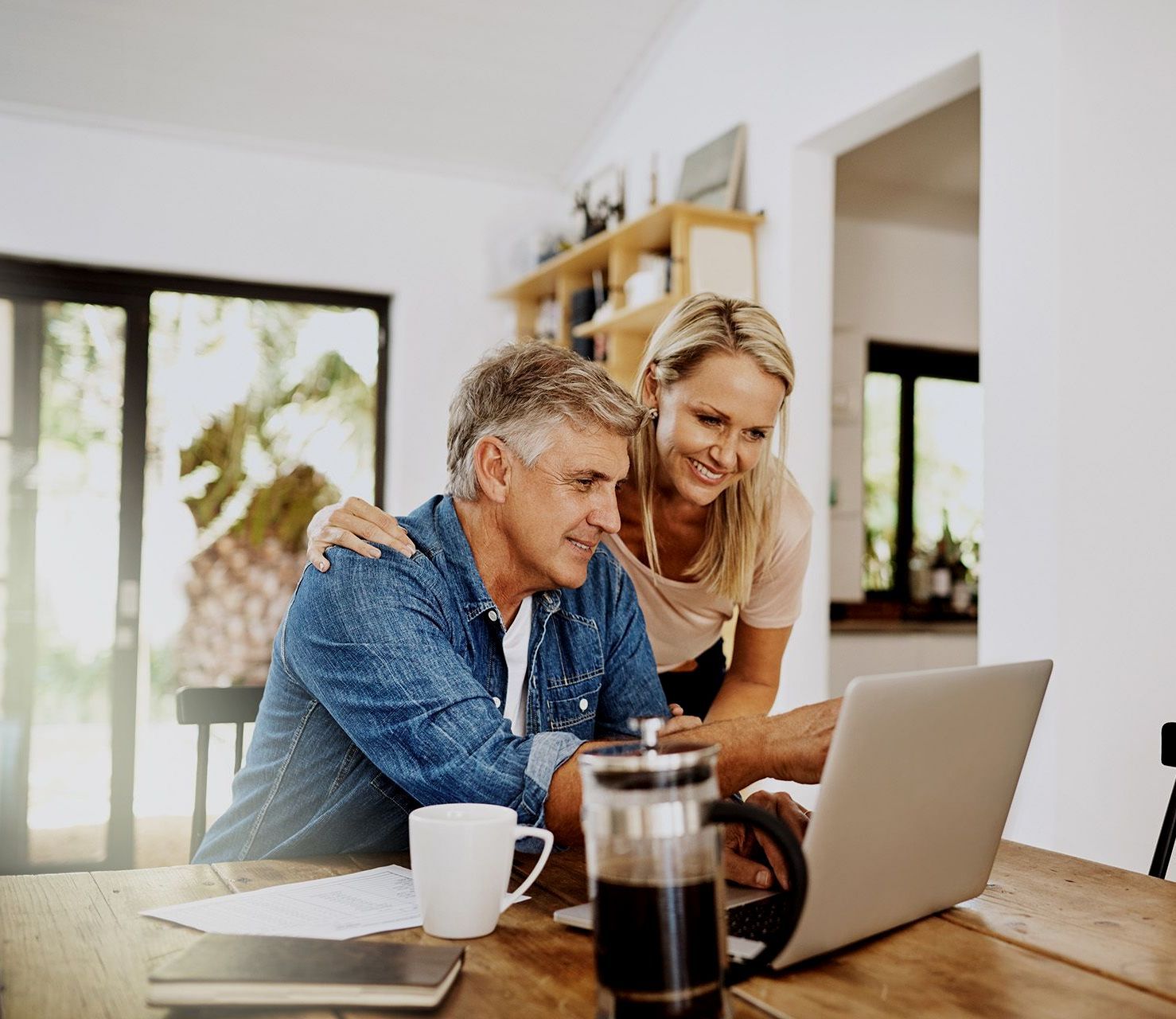 A man and a woman are sitting at a table looking at a laptop computer.