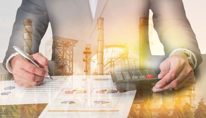 Person in business attire calculating finances, superimposed with industrial plant.