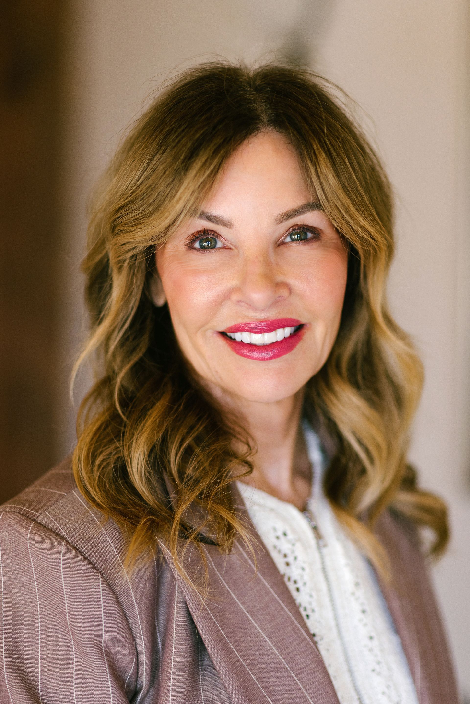 A woman wearing a blue turtleneck and a necklace is smiling for the camera.