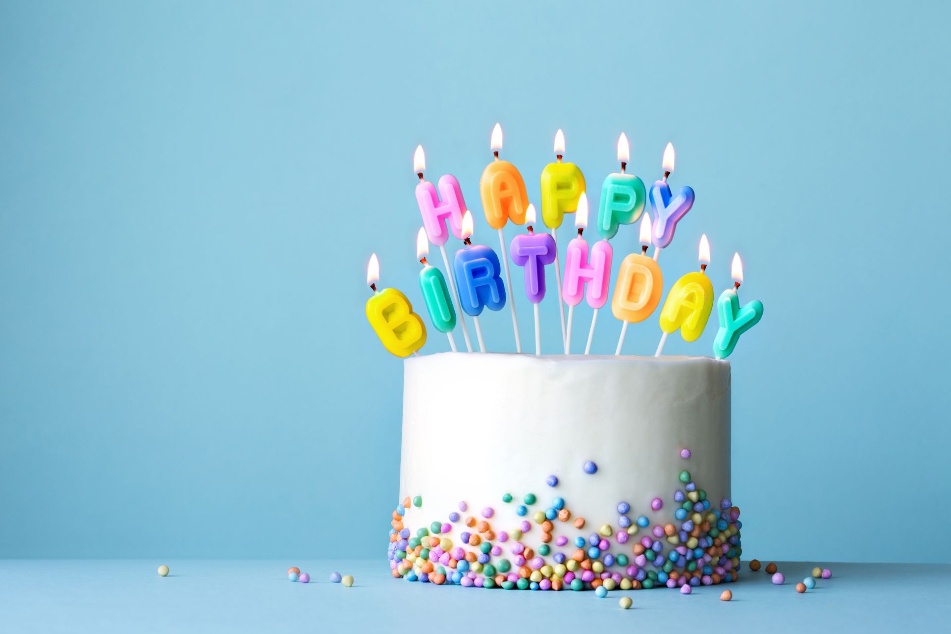 A birthday cake with colorful candles and sprinkles on a blue background.