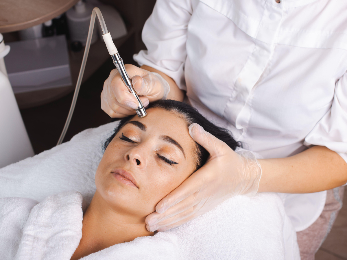 Woman receiving facial treatment, professional holding device to face, indoors.