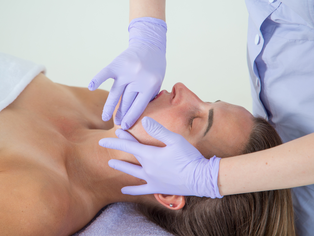 Person receiving facial massage; hands in blue gloves on face.