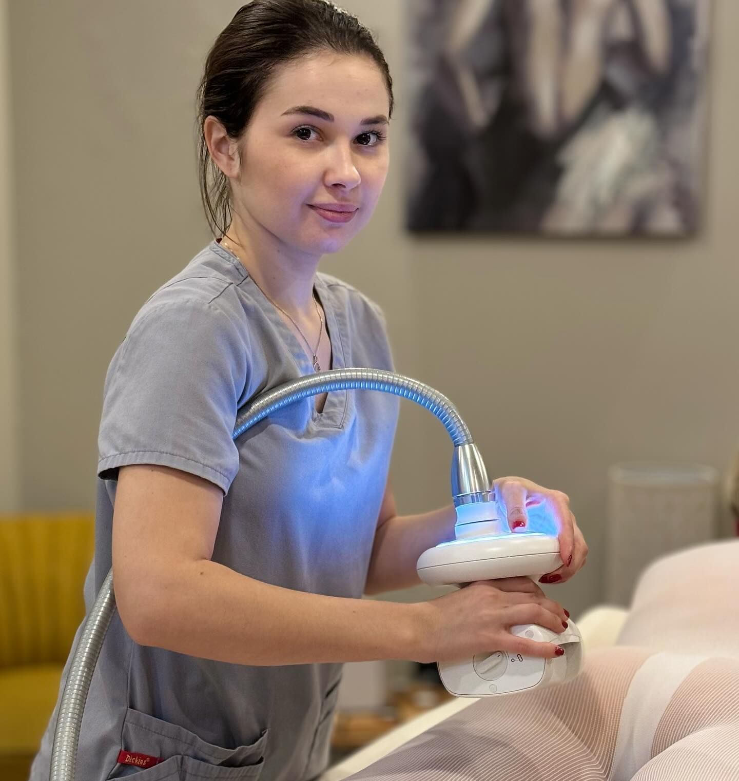 Woman in gray scrubs using a medical device on a patient in a clinic setting.