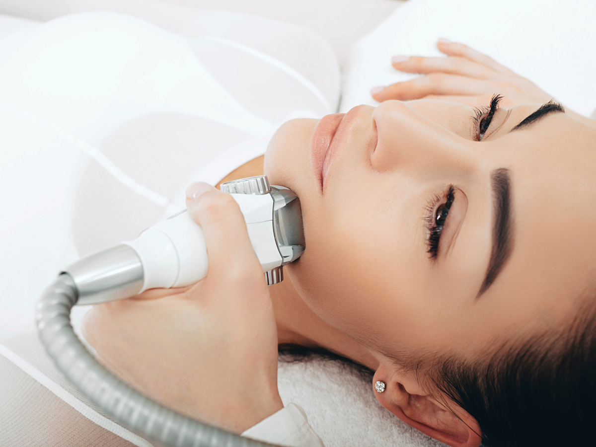 Woman receiving facial skin treatment, lying down. A device is being held to her jawline.