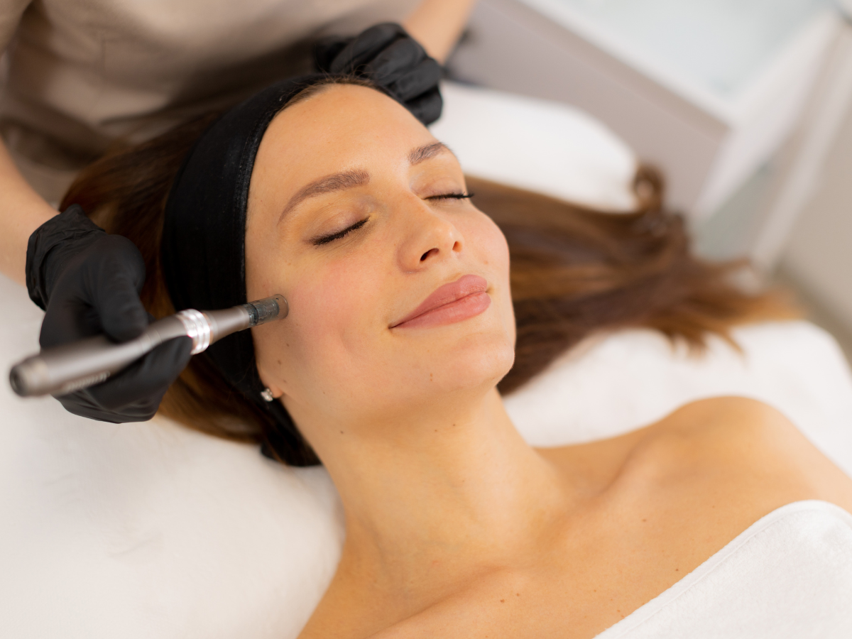Woman receiving facial treatment with closed eyes; hands with black gloves hold a tool.