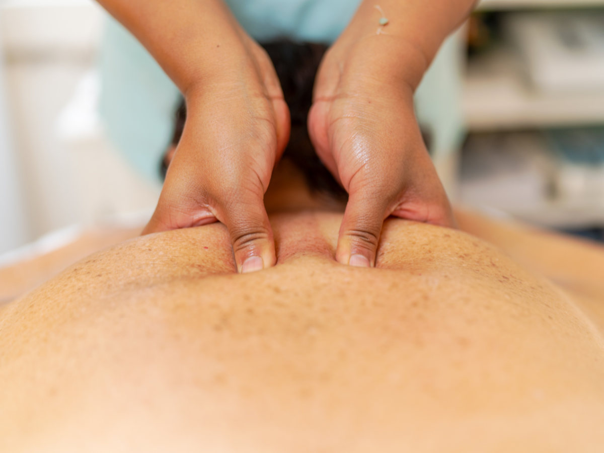 Hands massaging a person's upper back and neck, indoors.