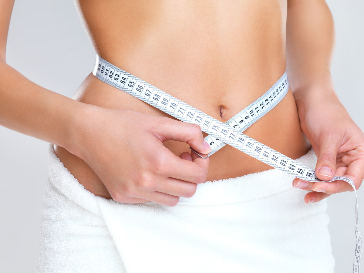Woman measuring waist with a white tape measure.