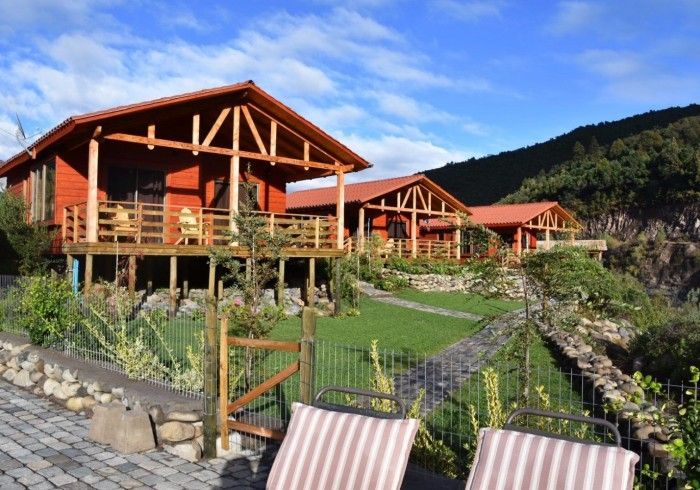 Cabañas de madera en la montaña, con techos rojos, con vistas a un jardín paisajístico y a las colinas.