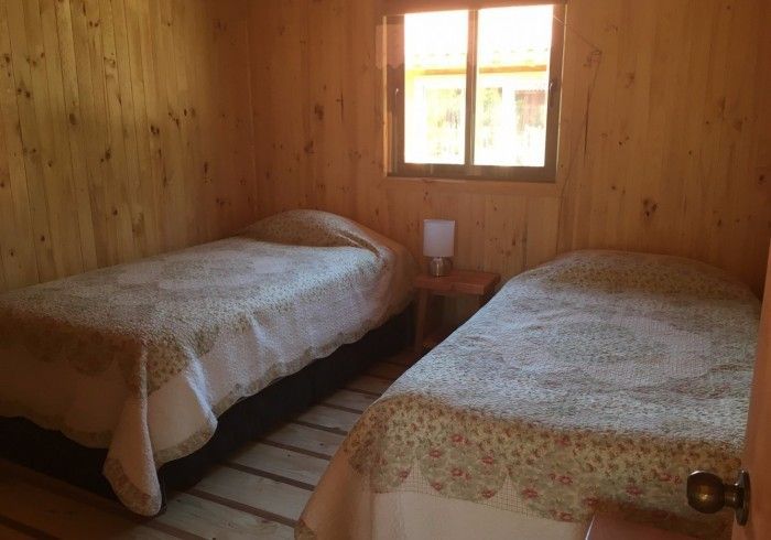 Pequeña habitación tipo cabaña de madera con dos camas individuales y una ventana que deja entrar la luz del día.