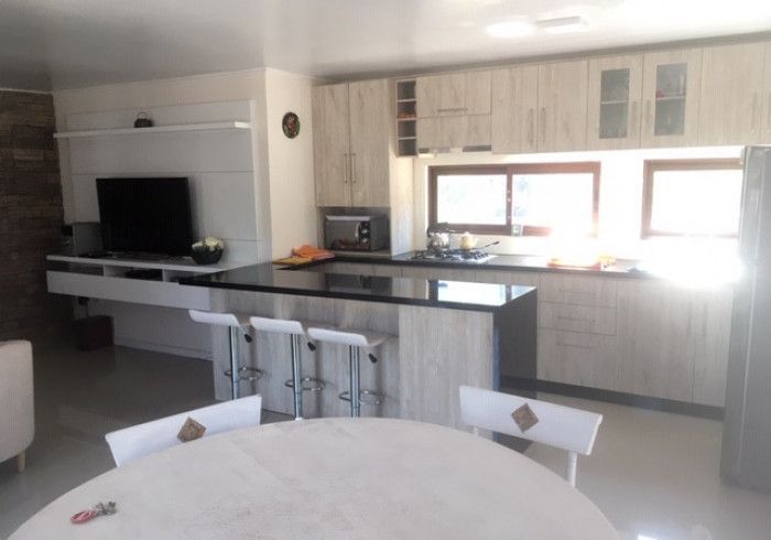 Cocina y sala de estar modernas y luminosas con isla, grandes ventanales y mesa de comedor redonda en primer plano.