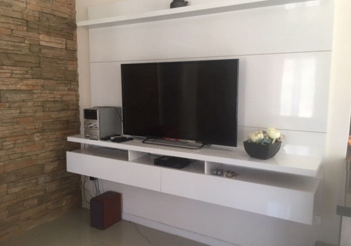 Mueble modular moderno para salón con televisor de pantalla plana, altavoces y cuenco decorativo sobre una repisa blanca.