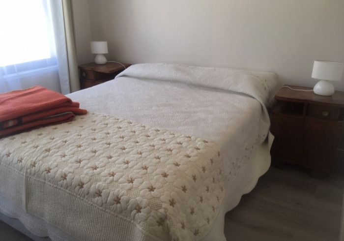 Una cama bien hecha con sábanas blancas, toallas rojas dobladas y lámparas de noche a juego en un dormitorio luminoso.