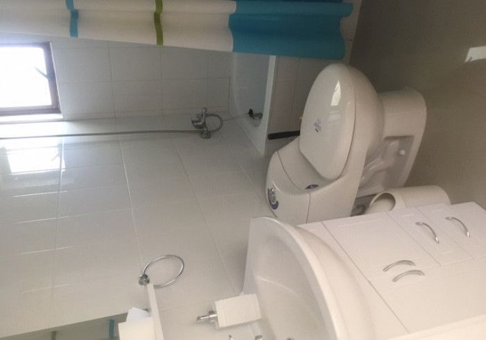 Baño con inodoro blanco, lavabo mural y ventana pequeña con persianas azules.