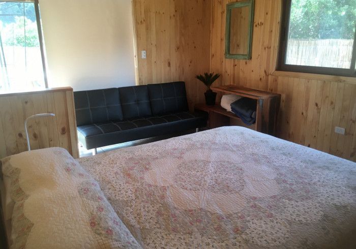 Dormitorio con una cama grande, sofá negro, paredes revestidas de madera y ventanas que dejan entrar la luz natural.