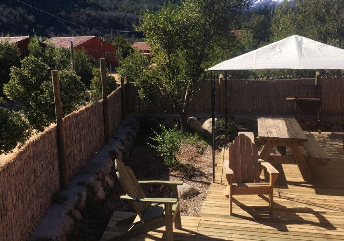 Terraza trasera con mesa de picnic, toldo blanco, valla, árboles y vistas a la montaña.