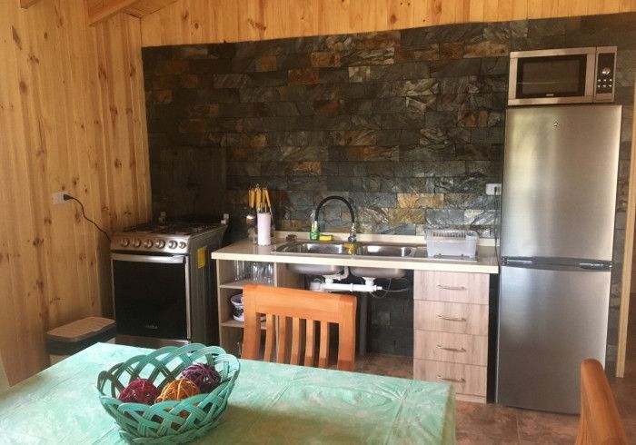 Cocina rústica con paredes de madera, salpicadero de piedra, fogones, fregadero, nevera y mesa de comedor.