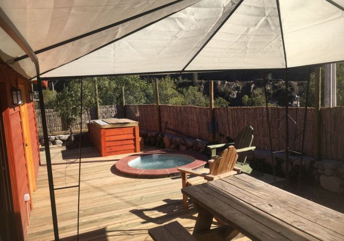 Terraza trasera con jacuzzi, banco de madera y un gran toldo.