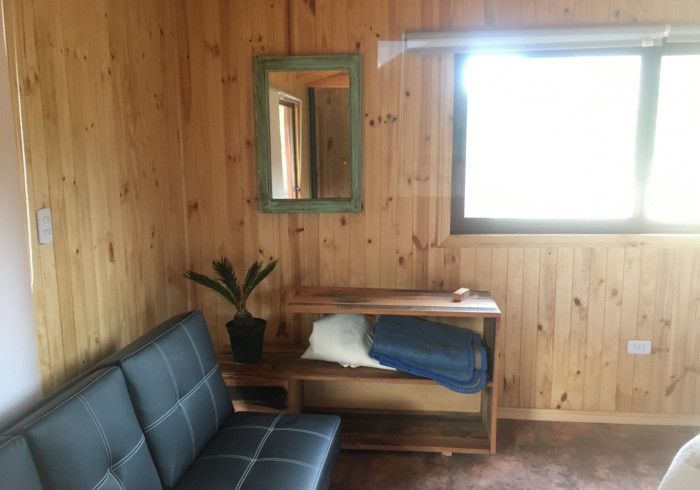 Habitación con paneles de madera, sofá negro, mesa pequeña, espejo, planta y ventana luminosa.