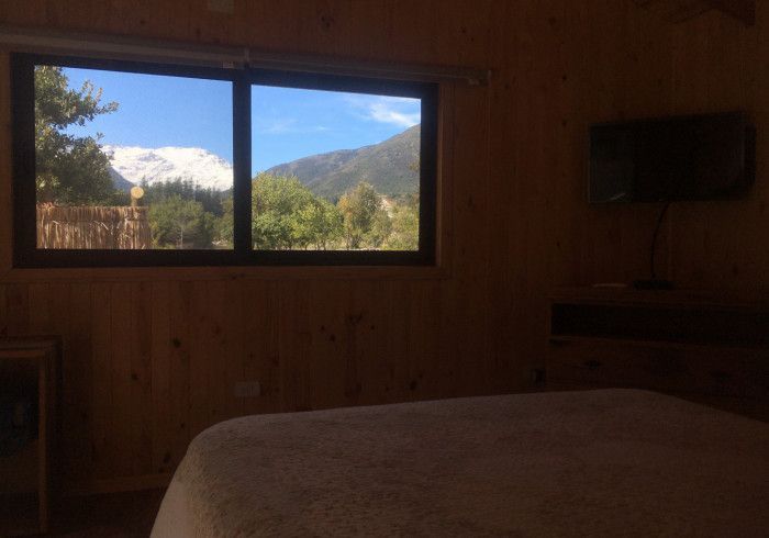 Dormitorio con paneles de madera y ventana con vistas a montañas nevadas y colinas verdes.
