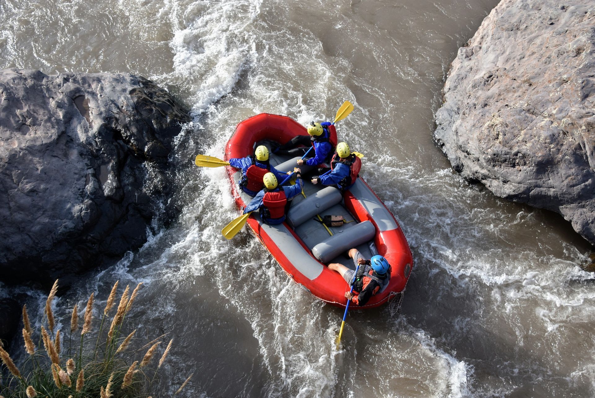 Balsa inflable roja que transporta a dos personas a través de las aguas turbulentas de un río entre grandes rocas.