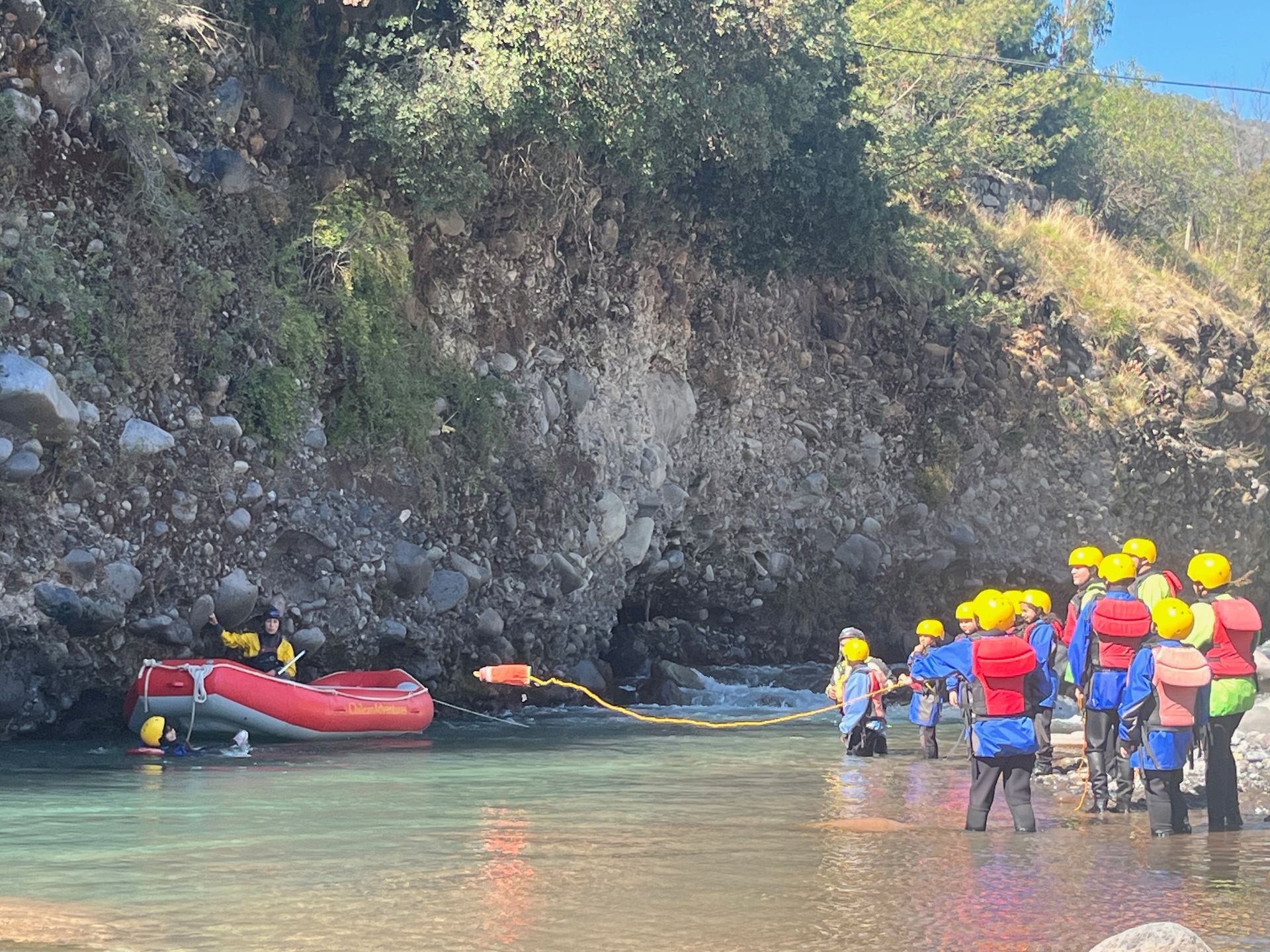 Un grupo de rafting en aguas bravas, con cascos y chalecos salvavidas, en una cala rocosa del río, con una balsa roja cerca.