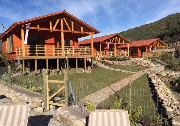 Cabañas de madera sobre pilotes con techos rojos y un sendero de piedra en un soleado complejo de montaña.