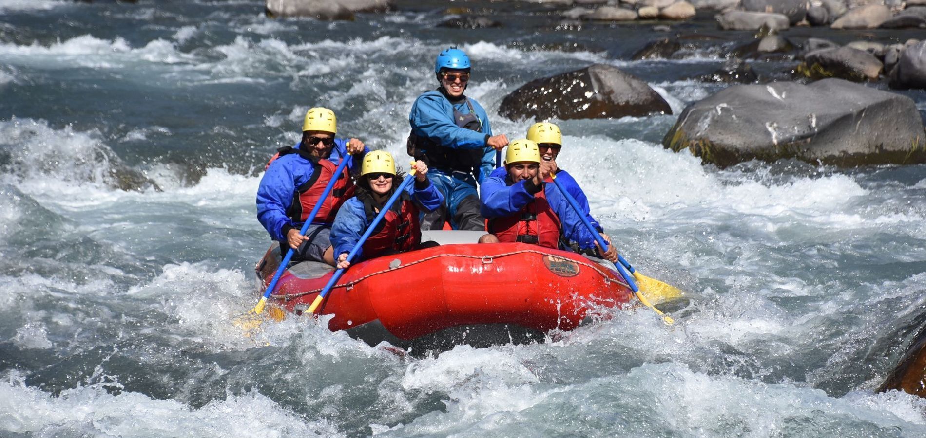 Un equipo de rafting con cascos azules rema en una balsa roja a través de rápidos.