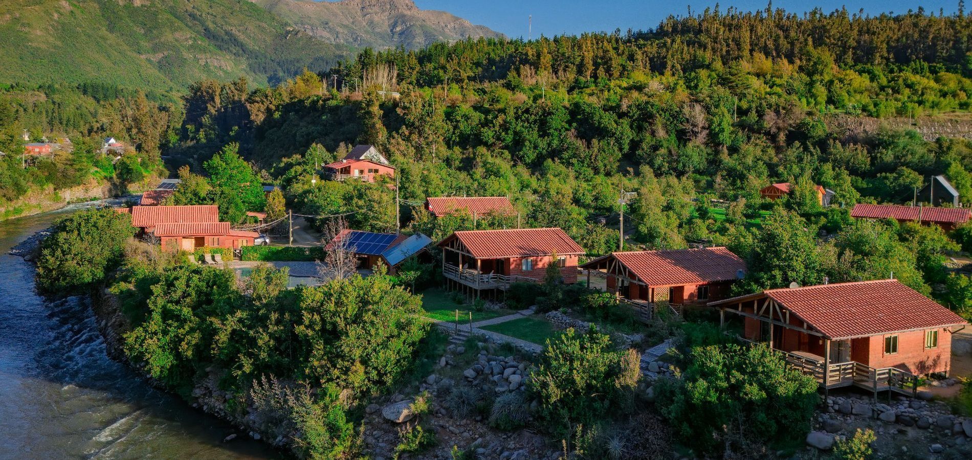 Complejo turístico en la ladera de una colina con villas de techos rojos rodeadas de un frondoso bosque verde y senderos serpenteantes.