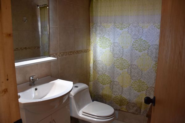 Baño pequeño con lavabo, inodoro y cortina de ducha con estampado floral, junto a una puerta de madera.