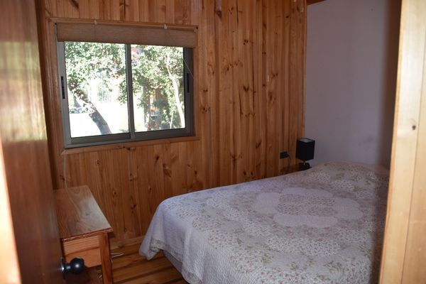 Habitación pequeña con paneles de madera, cama, ventana y cómoda.