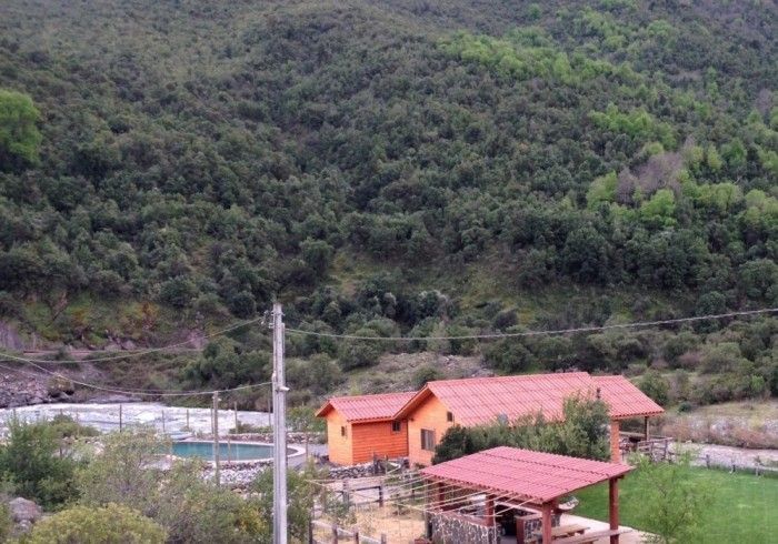 Pequeñas casas de color naranja junto a una carretera, con una exuberante ladera verde al fondo.