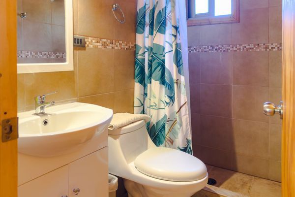 Baño pequeño con lavabo, inodoro, cortina de ducha y paredes alicatadas en color beige.